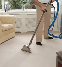 Professional carpet cleaner using a hot-water extraction wand and hose machine in a living room in Cincinnati, OH.