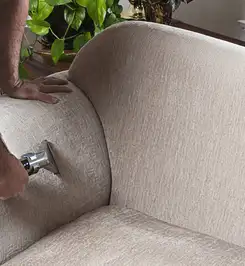 Professional upholstery cleaner deep-cleaning a fabric sofa with a handheld extraction tool and hose Cincinnati, OH.