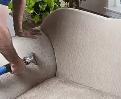 Professional upholstery cleaner deep-cleaning a fabric sofa with a handheld extraction tool and hose in Cincinnati, OH.